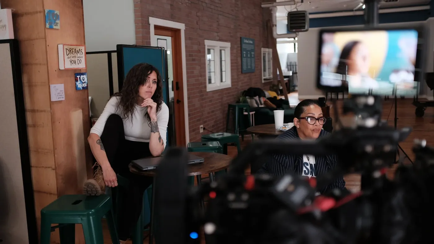 An interviewee seated on set, seen past the camera monitor