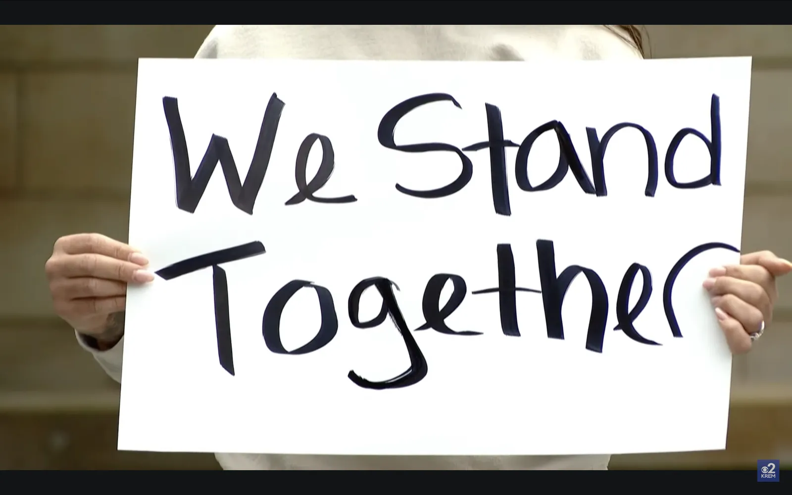 A hand-lettered sign reading “We Stand Together” held up at a rally